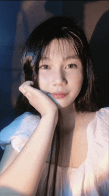 a woman with long black hair and a white shirt is holding her hand to her face
