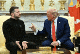 a man in a black shirt with the letter l on it talks to a man in a suit