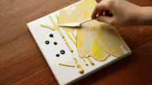 a person is using a spatula to spread yellow paint on a white canvas