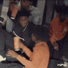 a group of young men are having a party and one of them is wearing an orange hoodie with the letter r on it .