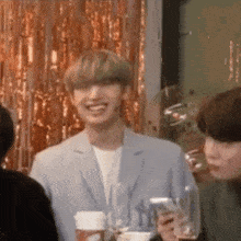 a man in a suit is smiling and holding a cup of coffee while standing in front of a group of people .