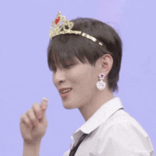 a young man wearing a tiara and earrings is licking his finger