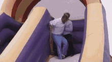 a couple of people are standing on top of a purple and yellow bouncy house .