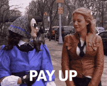 two women standing next to each other with pay up written on the sidewalk