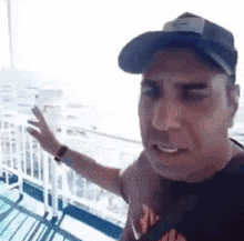 a man wearing a baseball cap and a t-shirt is standing next to a railing .