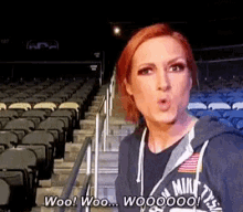 a woman in a hoodie is standing in an empty stadium and says woo