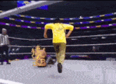 a man in a yellow shirt is running in a wrestling ring with the letters rcb on it