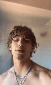 a young man with curly hair is wearing a necklace with the letter o on it