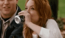 a woman is drinking soda from a can while a man looks on .
