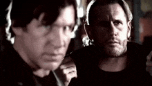 two men are standing next to each other in a dark room and looking at each other .