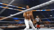 a man without a shirt is standing in a wrestling ring with a referee .