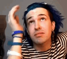 a man with blue hair is wearing a black and white striped shirt and earrings