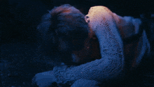 a man in a white sweater is laying on the ground in the dark