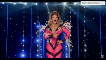 a drag queen in a pink outfit is on a stage with a watch in english advertisement