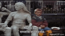 a little boy is sitting on a bench next to a statue .