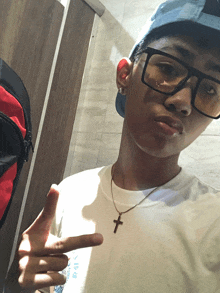 a young man wearing glasses and a cross necklace is giving a thumbs up sign