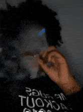 a man wearing a black shirt that says tuox on it is smoking a cigarette