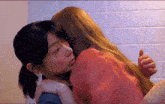 two women hugging each other in front of a white tiled wall