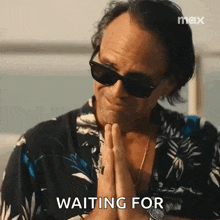 a man wearing sunglasses and a hawaiian shirt is praying with his hands folded .