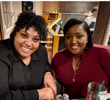 two women are sitting at a table smiling for a picture