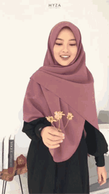 a woman in a purple hijab holds flowers in her hand