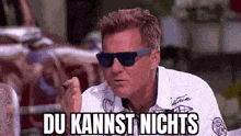 a man wearing sunglasses and a white shirt is making a funny face and says du kannst nichts .