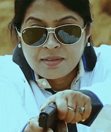 a woman wearing ray-ban sunglasses holds a gun in her hand