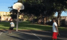 two men are playing basketball in a park and one of them is wearing red shorts