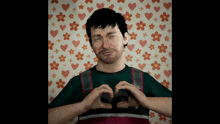 a man making a heart shape with his hands in front of a floral wallpaper