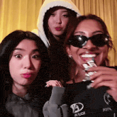 three women are posing for a picture and one of them is wearing sunglasses and a shirt that says ' a ' on it