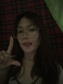 a woman wearing glasses and a plaid shirt is giving a peace sign