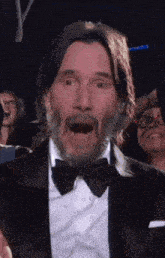 a man with a beard is wearing a tuxedo and bow tie and making a surprised face .