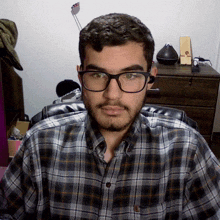 a man with glasses and a plaid shirt looks at the camera