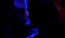 a man and a woman are kissing in a dark room with blue lights .