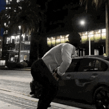 a man in a white shirt is standing next to a car with a palm tree in the background