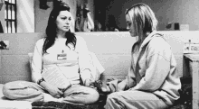 a black and white photo of two women sitting next to each other in a jail cell holding hands .