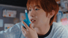 a young man with red hair is holding a blue toy walkie talkie
