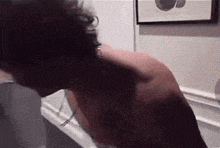 a man without a shirt is standing in front of a wall with a picture on it