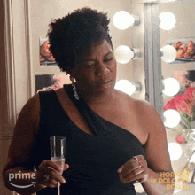 a woman in a black dress is holding a glass of champagne in front of a mirror that has the word prime on it