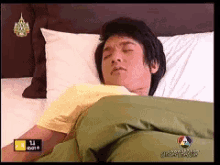 a man laying on a bed with a green blanket and a yellow shirt