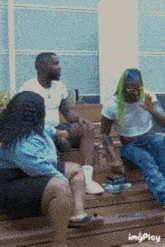 a group of people are sitting on a wooden bench and one of them has green hair ..