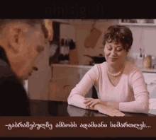 a woman in a pink sweater sits at a table with a man in a kitchen