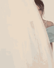a woman in a light blue dress and pearls is standing in front of a white curtain