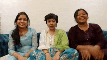 three women are sitting on a blue couch and smiling for the camera