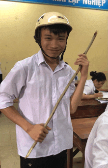 a boy wearing a helmet and holding a stick stands in front of a sign that says ' lập nghiệp '