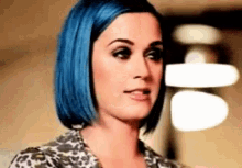 a woman with blue hair is wearing a leopard print top .