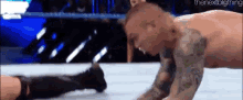a man is laying on the ground in a wrestling ring while another man kicks him .