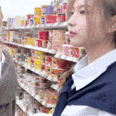 a woman is standing in front of a shelf full of ramen cups including one that says ' ramen ' on it
