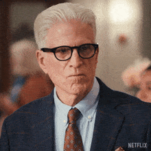 a man wearing glasses and a suit has a netflix logo on his shirt pocket