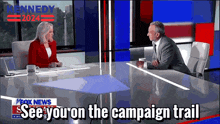 a man and a woman are sitting at a table in front of a fox news sign that says see you on the campaign trail